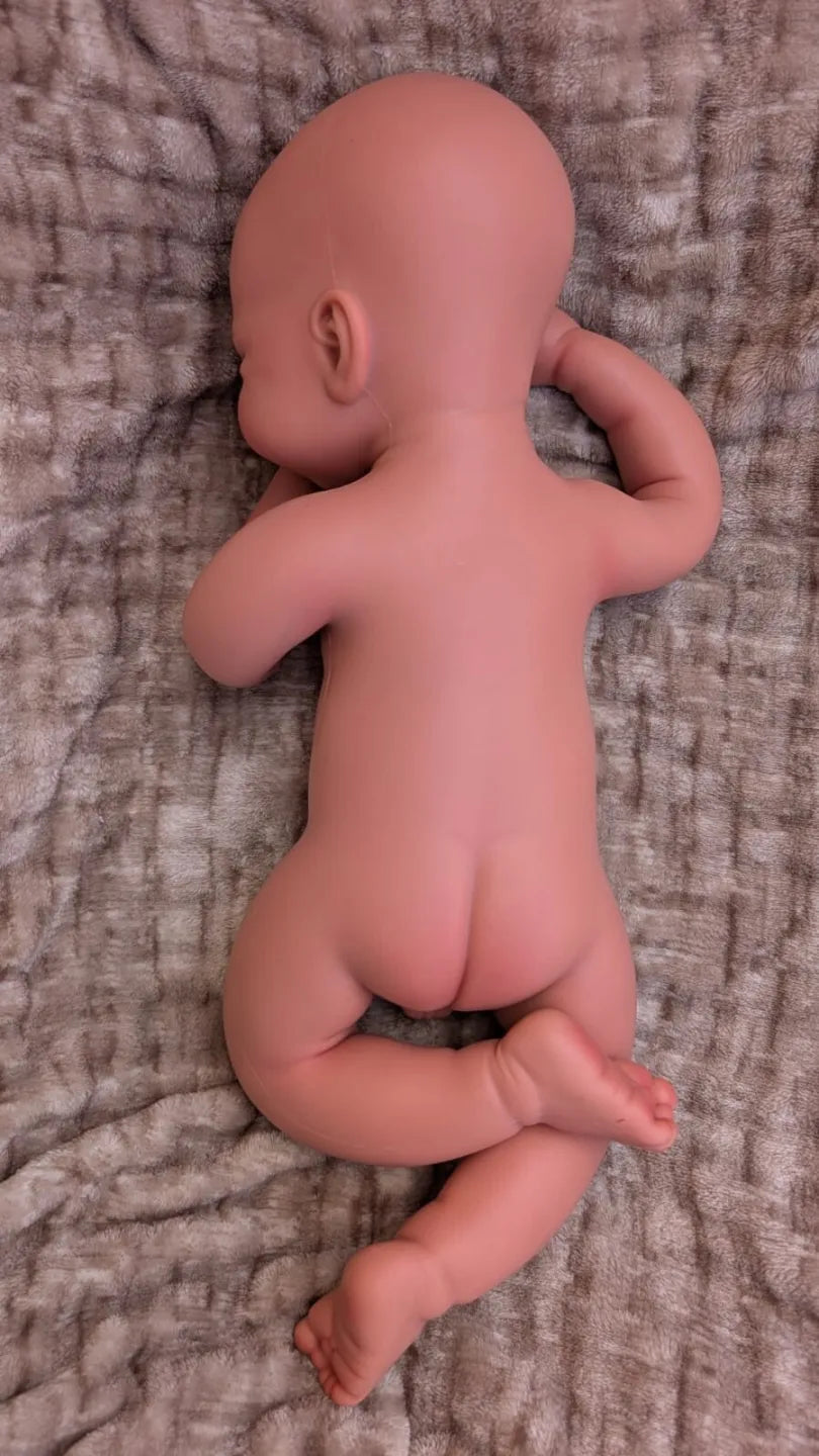 vista di dietro della bambola reborn nuda di 50cm in posizione appena nato con le gambe piegate
