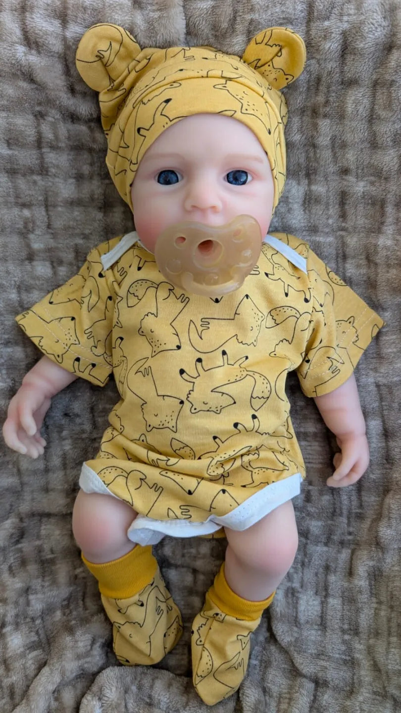bambola reborn con vestiti da neonato gialli e ciuccio nella bocca
